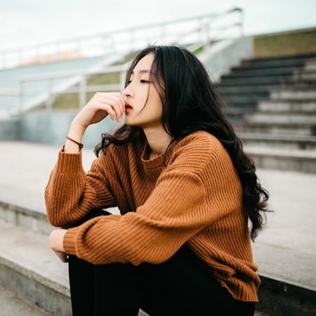 woman in rust colored sweater looking contemplative sitting on stairs