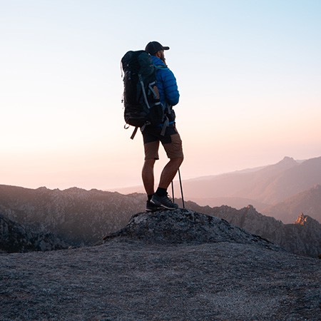 Man in hiking gear standing at overlook during sunset
