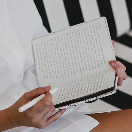 Woman journaling in white shirt on black and white striped couch