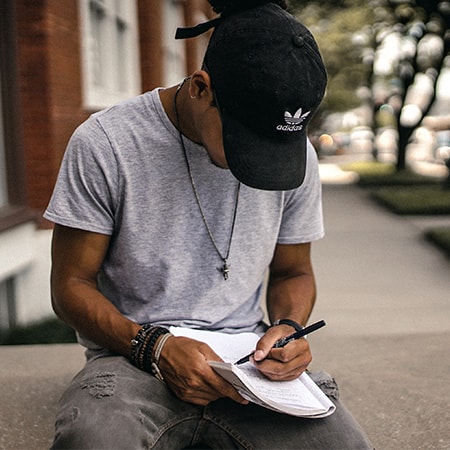Man in gray shirt and black hat writing in journal